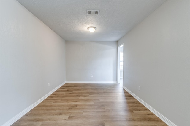 spare room with a textured ceiling, light wood-style flooring, visible vents, and baseboards