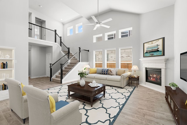 11926 Maple Oak Dr, Houston, TX 77066 - living room featuring ceiling fan, a towering ceiling, a glass covered fireplace, light wood-style floors, and stairs
