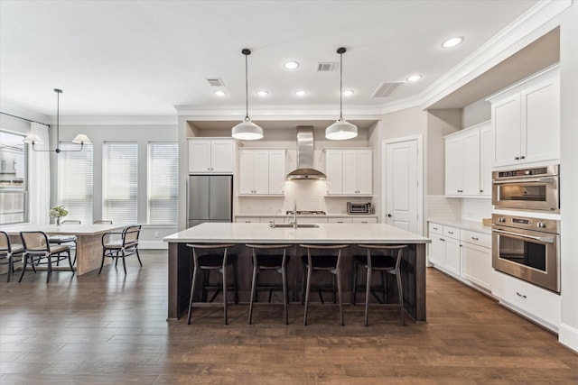 kitchen featuring visible vents, appliances with stainless steel finishes, a kitchen breakfast bar, wall chimney range hood, and a sink