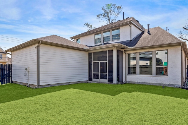 rear view of house with brick siding, fence, a sunroom, a yard, and roof with shingles