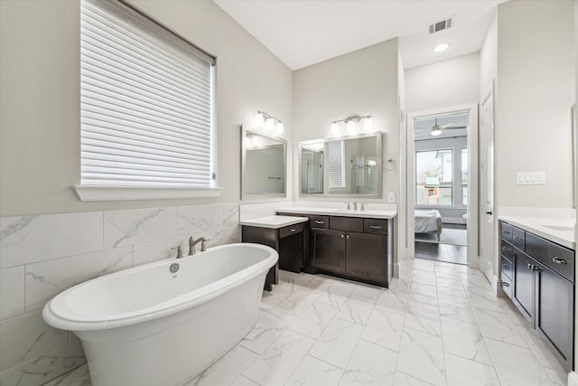 bathroom featuring marble finish floor, two vanities, visible vents, a sink, and a freestanding tub