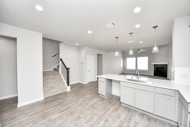 kitchen with wood finish floors, visible vents, a sink, a fireplace, and light countertops