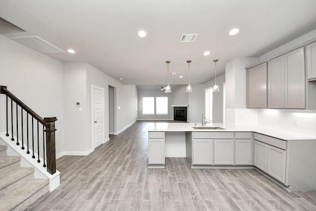 kitchen featuring visible vents, gray cabinetry, light wood-style flooring, a sink, and open floor plan