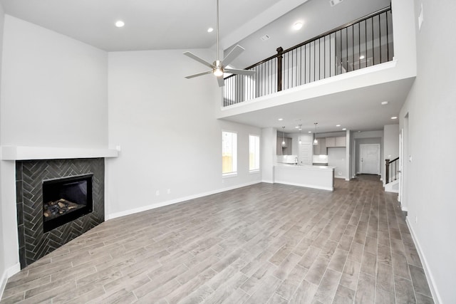 unfurnished living room with baseboards, a ceiling fan, wood finished floors, and a tiled fireplace