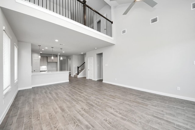 unfurnished living room with stairway, baseboards, visible vents, and wood finished floors