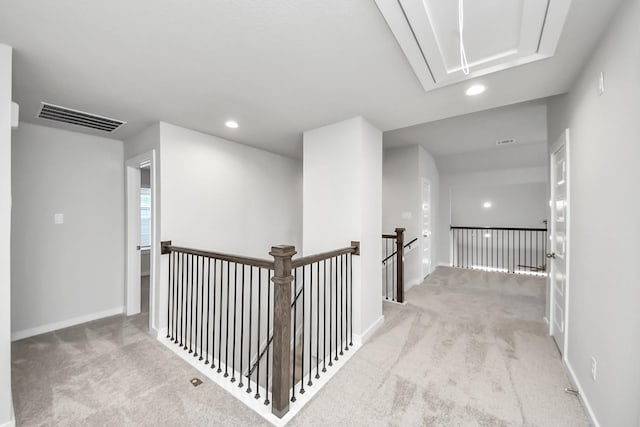 hallway with an upstairs landing, visible vents, attic access, and carpet floors