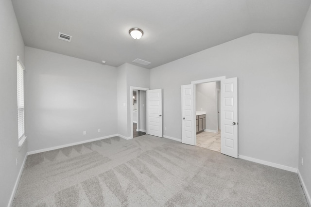 unfurnished bedroom with visible vents, baseboards, carpet, lofted ceiling, and ensuite bath