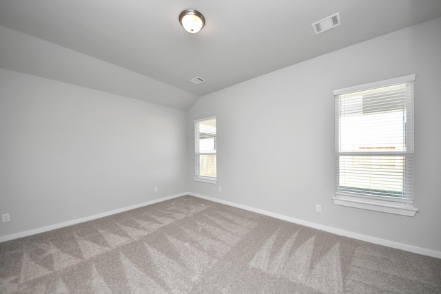 empty room with carpet flooring, visible vents, baseboards, and lofted ceiling