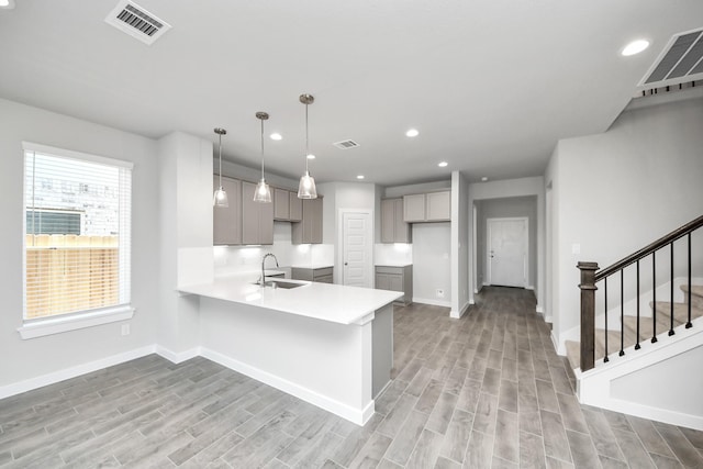 kitchen with light wood finished floors, visible vents, a peninsula, and a sink