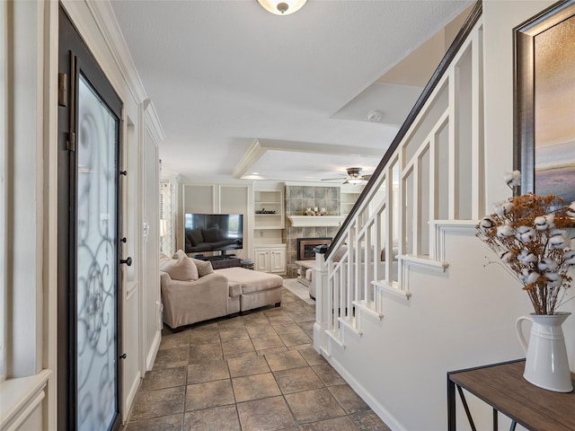 entryway featuring a large fireplace, ceiling fan, stairway, and crown molding