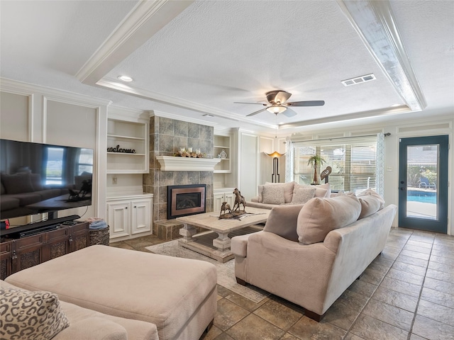 living room with ornamental molding, a tray ceiling, a textured ceiling, and a fireplace