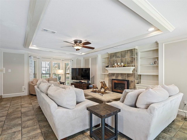 living area with visible vents, a ceiling fan, a tiled fireplace, ornamental molding, and a tray ceiling