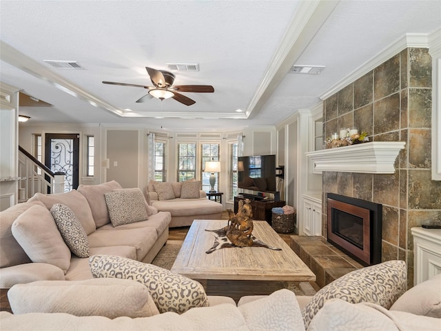 living room featuring a tiled fireplace, a raised ceiling, visible vents, and crown molding