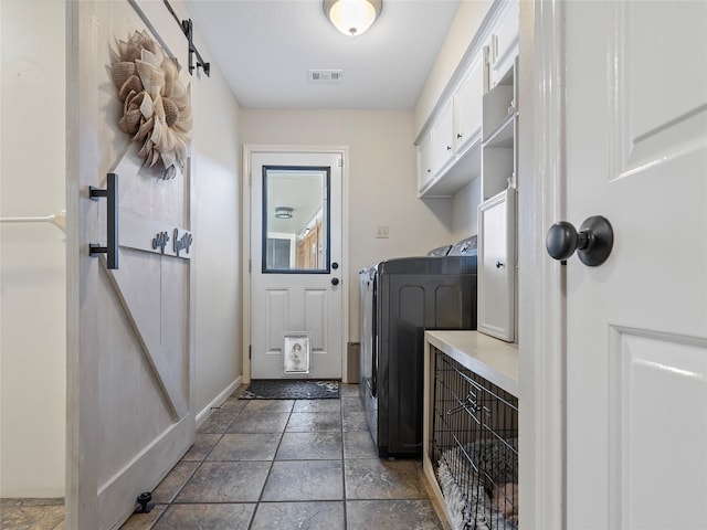 mudroom featuring stone finish flooring, visible vents, washing machine and clothes dryer, and a barn door