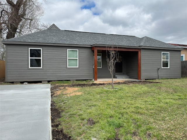 rear view of house with a yard, roof with shingles, and fence