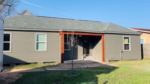 back of house featuring entry steps, a yard, a shingled roof, and fence