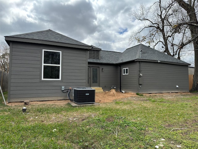 back of property with a shingled roof, a lawn, and central air condition unit