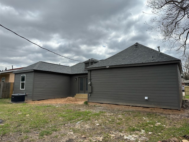 rear view of house featuring central AC, fence, entry steps, and a shingled roof