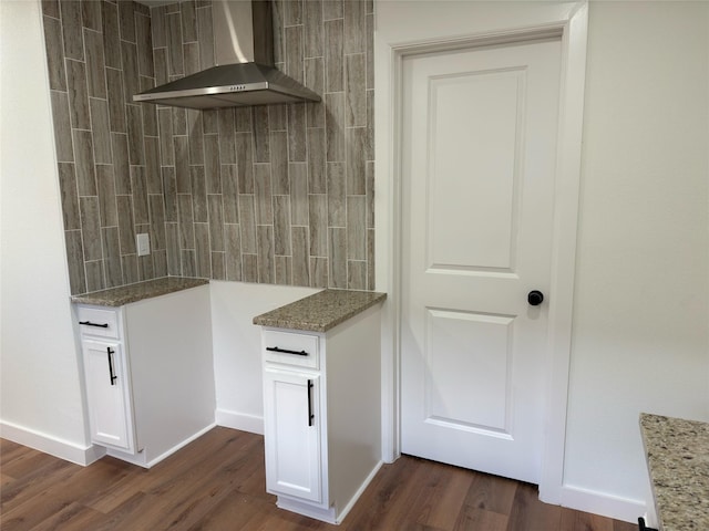 kitchen featuring wall chimney range hood, dark wood finished floors, light stone counters, and white cabinets