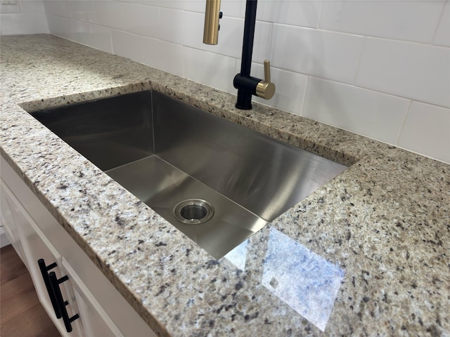 interior details with dark wood-style flooring, a sink, light stone countertops, and decorative backsplash