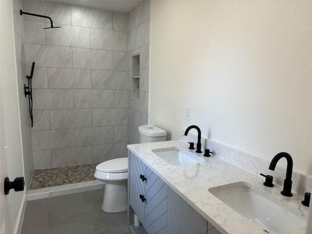 full bathroom with toilet, double vanity, a sink, and tiled shower