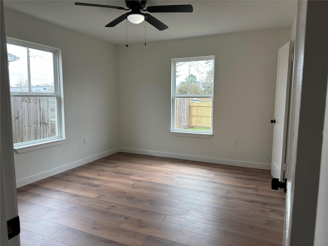 spare room with a healthy amount of sunlight, a ceiling fan, baseboards, and wood finished floors