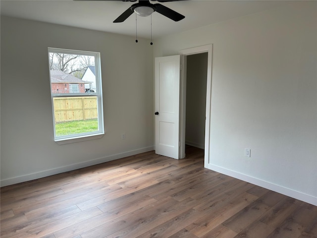 empty room with wood finished floors, a ceiling fan, and baseboards