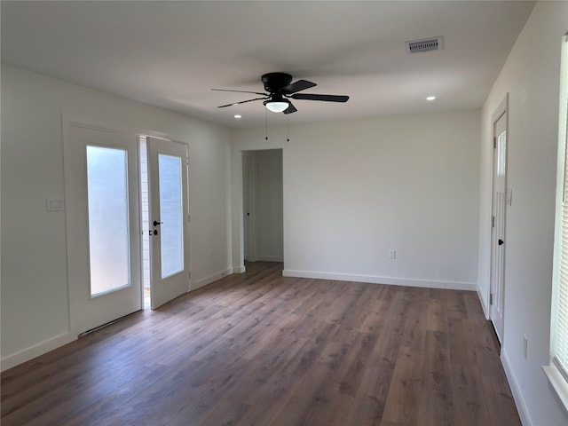 empty room featuring dark wood-type flooring, visible vents, baseboards, and a ceiling fan