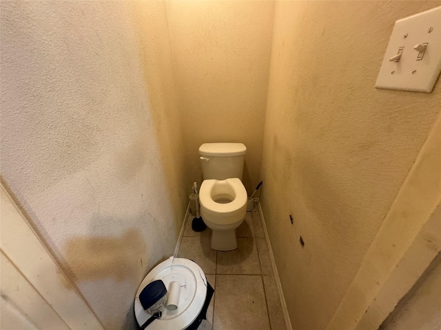 bathroom with a textured wall, tile patterned flooring, toilet, and baseboards