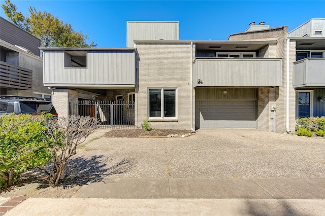 rear view of property with a garage, driveway, a balcony, fence, and brick siding