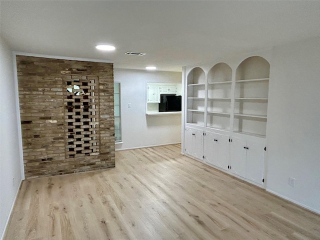 unfurnished room featuring light wood-style floors, visible vents, and built in shelves