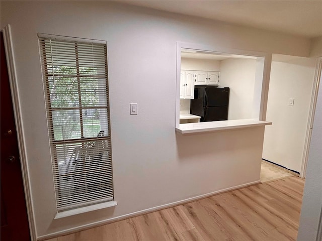 kitchen with light countertops, light wood-style flooring, freestanding refrigerator, white cabinets, and a peninsula