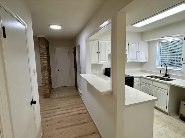 kitchen with black electric range, light countertops, white cabinets, a sink, and a peninsula