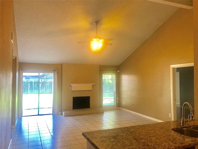 unfurnished living room featuring a fireplace with raised hearth, ceiling fan, high vaulted ceiling, a sink, and light tile patterned flooring