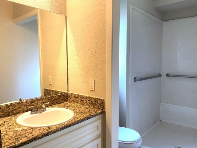 bathroom with a textured wall, vanity, and toilet