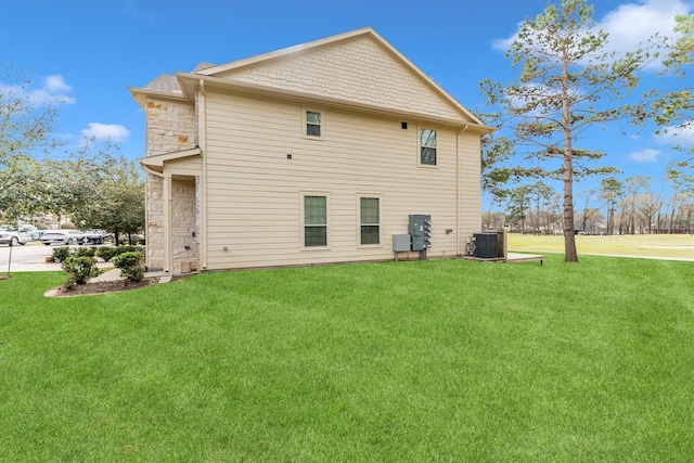 rear view of property with a yard, stone siding, and central AC