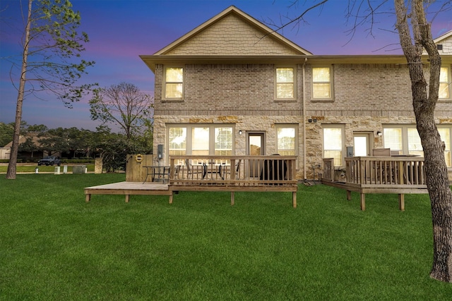 back of house at dusk featuring a wooden deck, a lawn, and brick siding