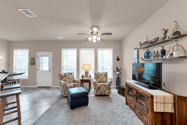 living area with light tile patterned floors, visible vents, ceiling fan, and baseboards