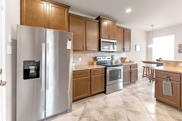 kitchen featuring tasteful backsplash, hanging light fixtures, appliances with stainless steel finishes, and light stone countertops