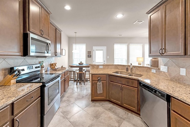 kitchen with visible vents, a sink, light stone counters, stainless steel appliances, and a peninsula