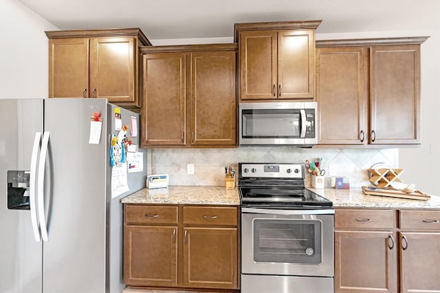 kitchen with tasteful backsplash, brown cabinets, appliances with stainless steel finishes, and light stone countertops