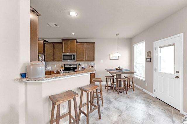 kitchen with visible vents, a peninsula, stainless steel appliances, a kitchen bar, and backsplash