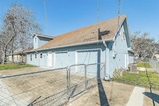 view of side of home with a garage, roof with shingles, fence, central air condition unit, and stucco siding