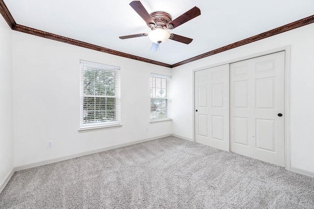 unfurnished bedroom with ceiling fan, baseboards, ornamental molding, a closet, and carpet