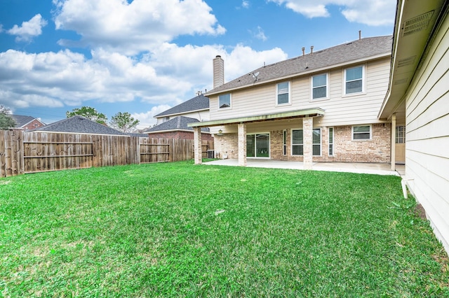 back of property with brick siding, a patio, a chimney, a lawn, and a fenced backyard