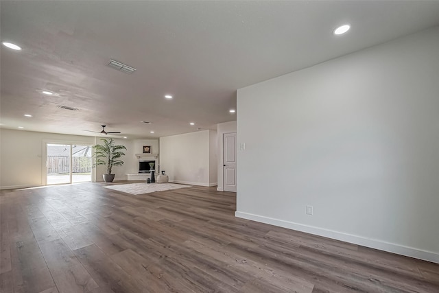 unfurnished living room with a fireplace with raised hearth, dark wood-type flooring, visible vents, baseboards, and a ceiling fan