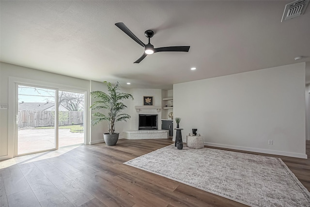 living area featuring baseboards, visible vents, a ceiling fan, wood finished floors, and a fireplace