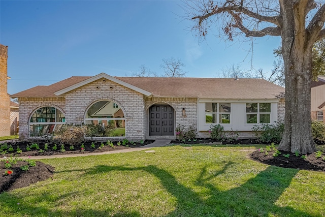 view of front of property with a shingled roof, a front lawn, and brick siding