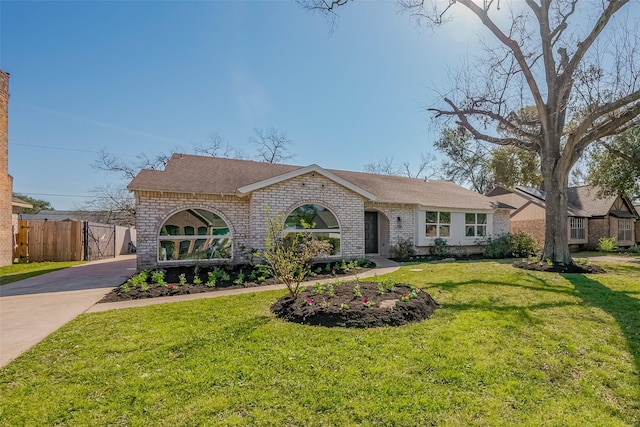 view of front of property with brick siding, a shingled roof, fence, driveway, and a front lawn