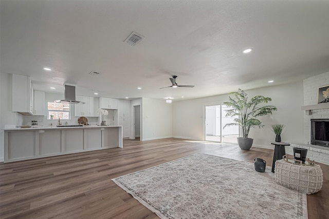 living area featuring ceiling fan, a brick fireplace, wood finished floors, and visible vents